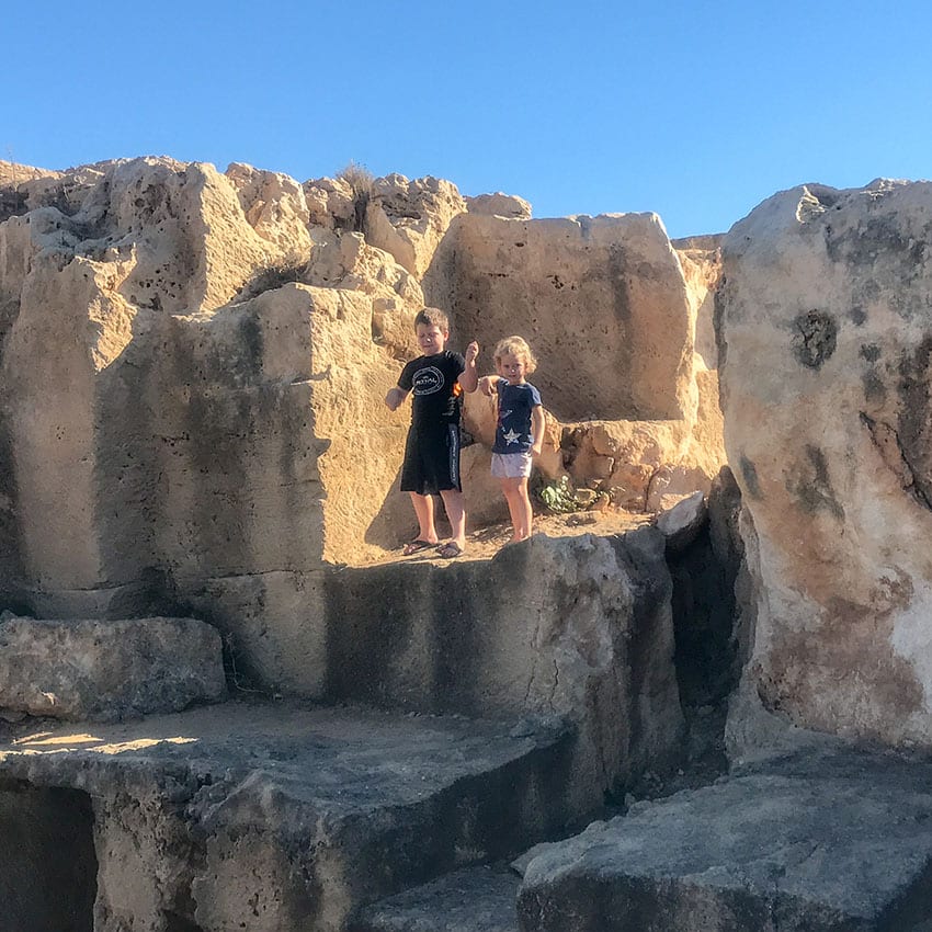 two young children standing on ruins at the Tombs of the Kings in Cyprus