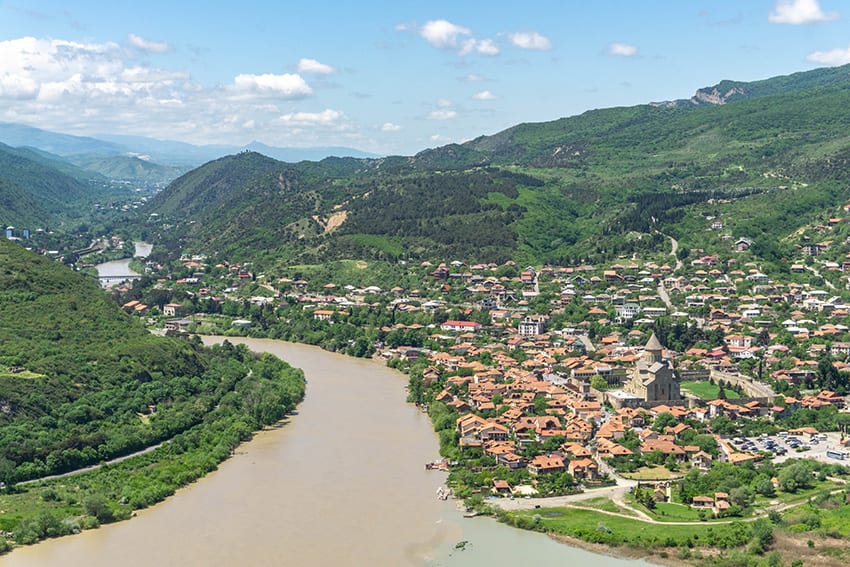 Mtskheta in Georgia - a long winding river with a town on the right hand side and green hills beyond 