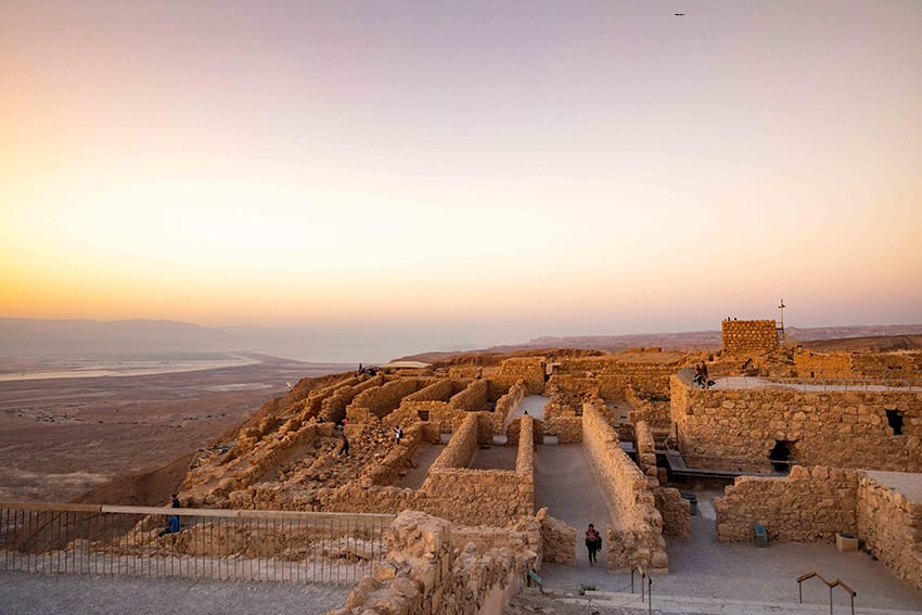 8 Amazing UNESCO Sites in The Middle East - Off the Beaten Track 5 the ruins of Masada Fortress with the sun rising in the background. The walls show the rectangular layout of the rooms in the fort.