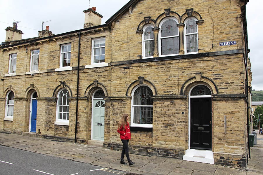 Guide to 17 Amazing UNESCO Heritage Sites in the UK 12 Girl with long brown hair wearing a red coat, black trousers and boots walking down a street called Titus St.