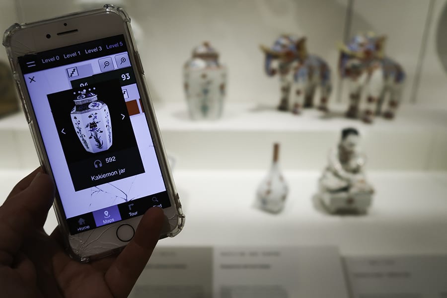 The British Museum, London - 30 Top Tips For Your Visit 3 Mobile phone screen showing a vase with actual pottery vase, elephants and figurines in the background