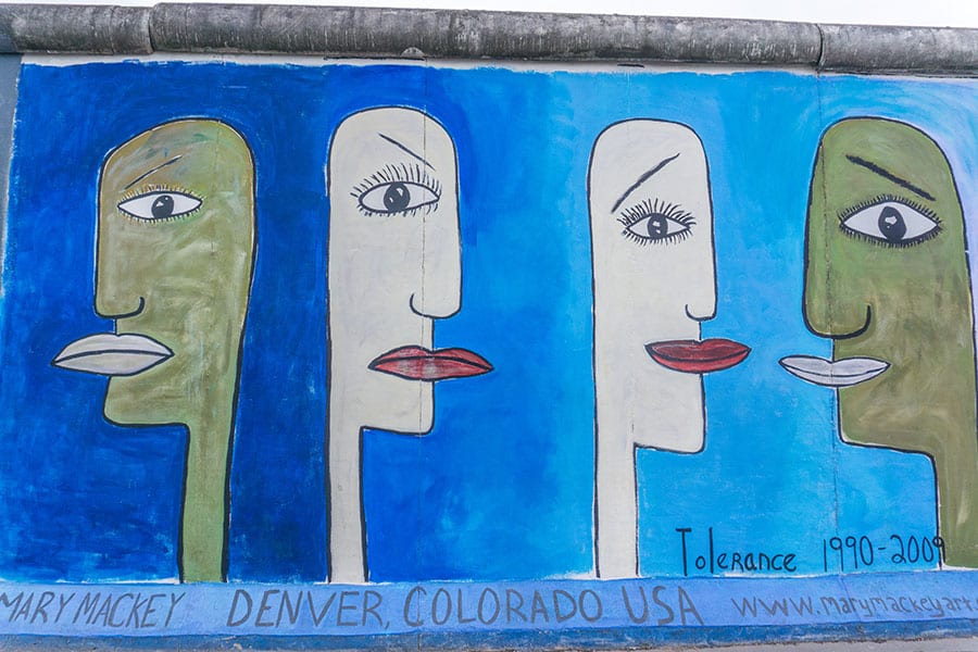 Part of the Berlin Wall which you can see one of the Day trips from Hamburg The wall is painted blue with faces painted on it. Two unsmiling faces facing away from each other and two smiling faced facing each other. Tolerance 1990 -2009 and Mary Mackey Denver Colarado USA on the bottom