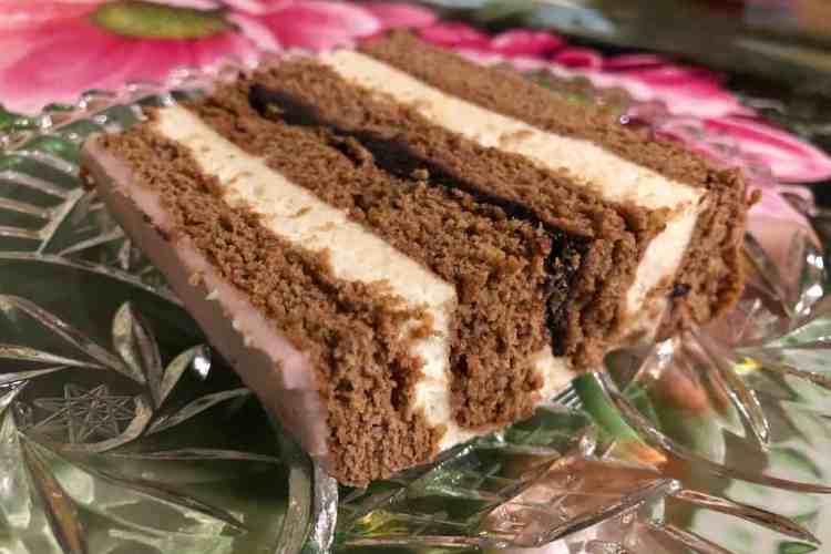 A glass plate with piernik - a polish gingerbread - on it with layers of semolina custard, gingerbread and pink frosting on top