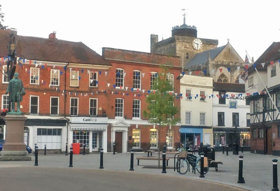 Market square with a Romsey Abbey in the background. There is blue, red and white bunting between the buildings
