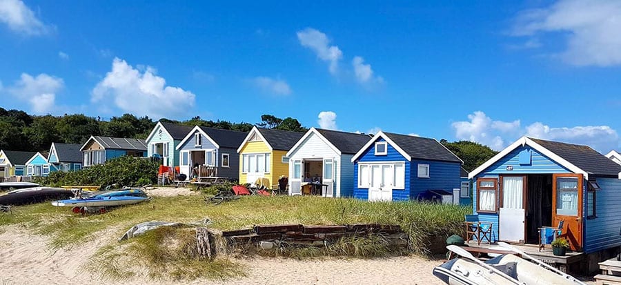 10+ of the Best Weekends in Dorset 4 A row of different painted beach huts with grass and sand in front