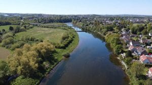 aerial view over the river Tweed with green fields on the left and houses on the right
