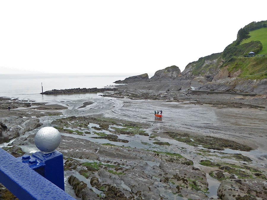 10+ of the Best Weekends in Devon 11 beach at Coombe Martin with tide out and 3 men taking an orange kayak out to sea