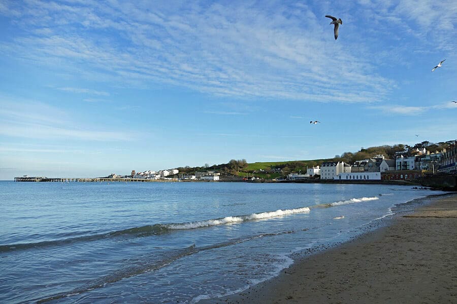 10+ of the Best Weekends in Dorset 12 The beach at Swanage with the tide coming in and white houses in the background and blue skies.