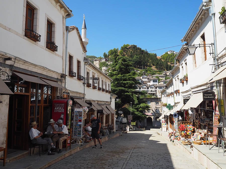 street in Gjirokastra with white buildings either side and souvenirs on the pavement under awnings