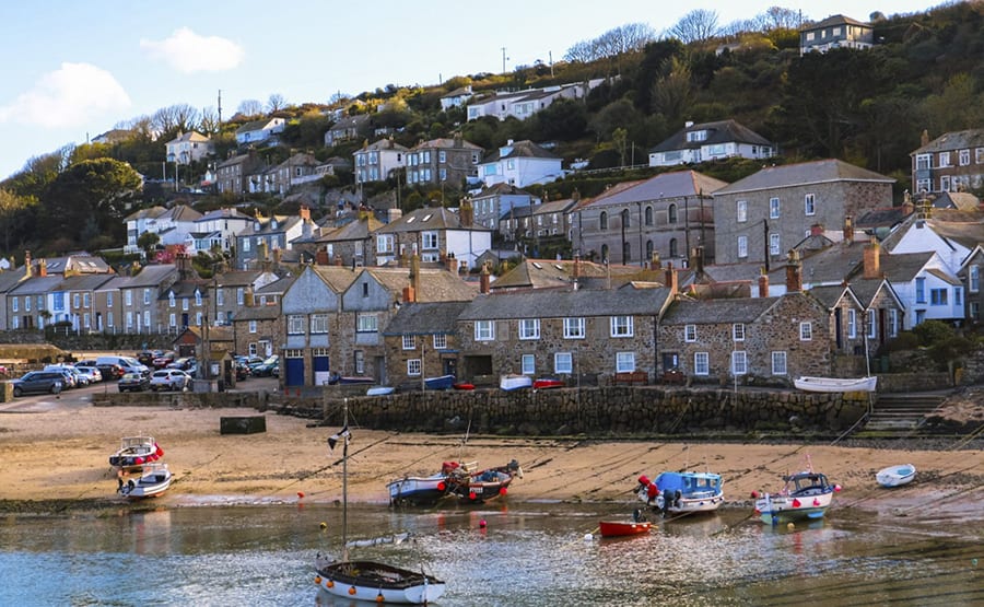 25 Amazing Hidden Gems in England and Wales to discover 23 rows of houses going up a hill with a sandy beach in the foreground with boats on it