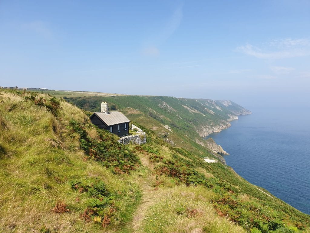 25 Amazing Hidden Gems in England and Wales to discover 11 black wooden house sitting on the cliffside over looking the sea on Lundy Island