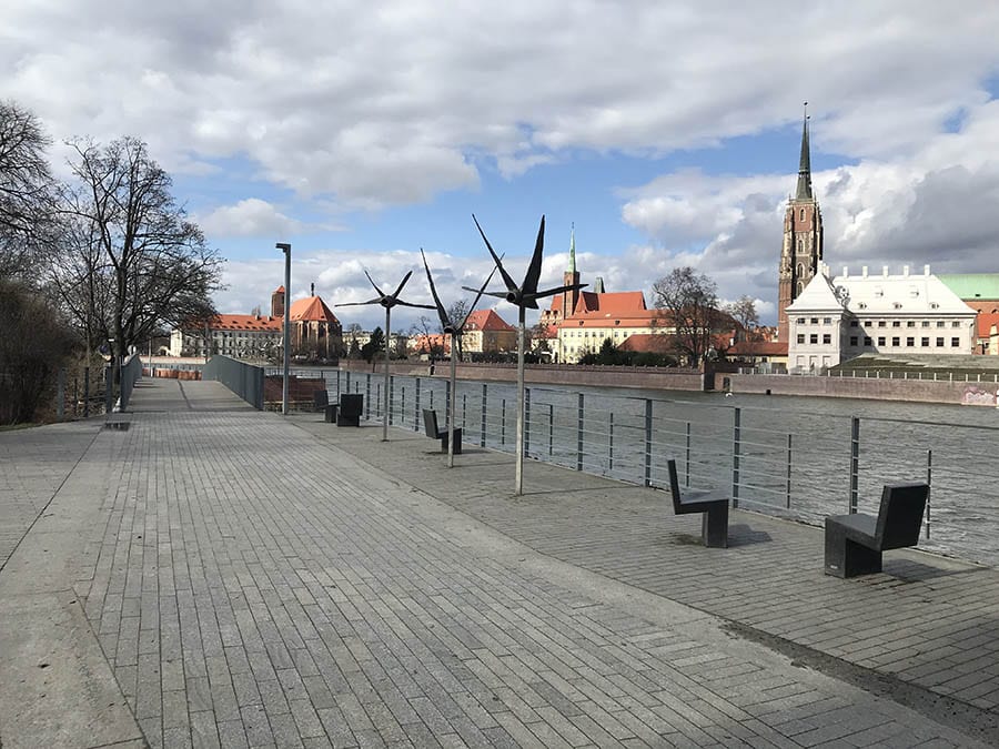 Wroclaw, a hidden gem in Poland - image shows a riven with walkway to the left and churches and other red roofed buildings on rightt