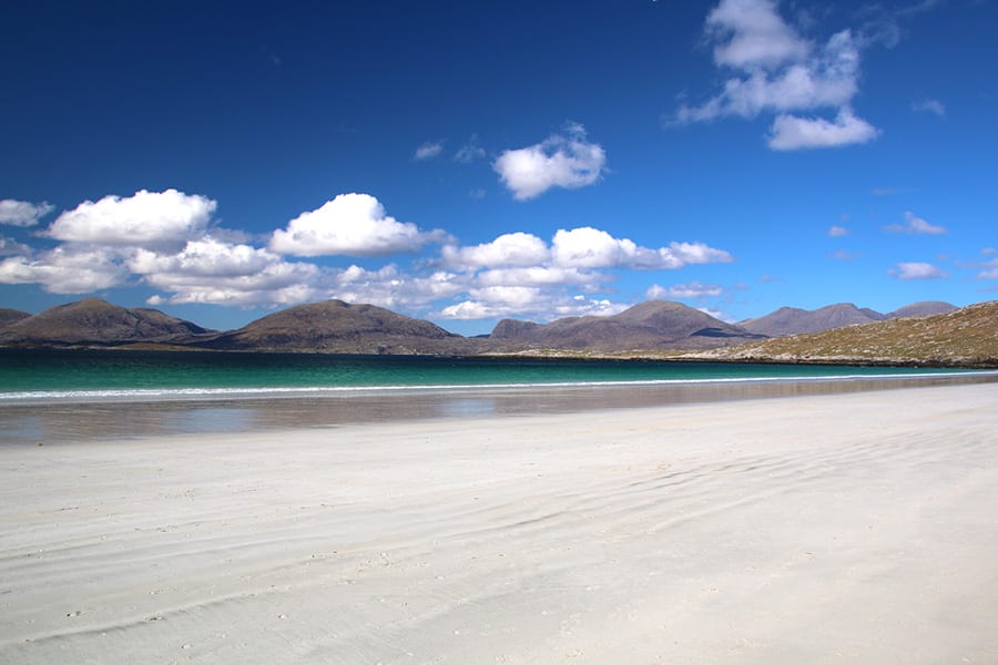 white sandy beach with green sea and hills in the background