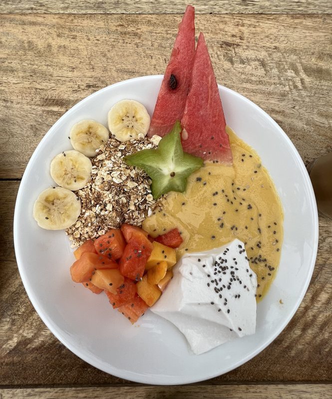 19 Awesome Vegan Restaurants around the World 2 white bowl filled with sliced bananas and starfruit, diced guava, triangles of watermelon, muesli, thick fruit smoothie and vegan coconut yoghurt
