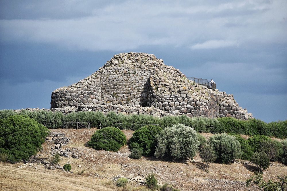 grey stone round semi-derelict structure with dark green scrub bushes in front