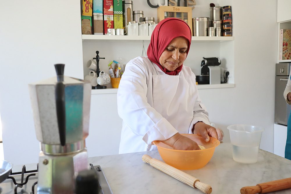 Sawa Taste Of Tunisia: Explore The Amazing Food Of Tunisia 5 Lady called Moufida wearing a white apron and a red head scarf making mwali dough in an orange bowl