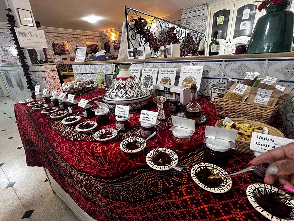 Sawa Taste Of Tunisia: Explore The Amazing Food Of Tunisia 9 selection of harissas in black and white small dishes with a large tagine behind them