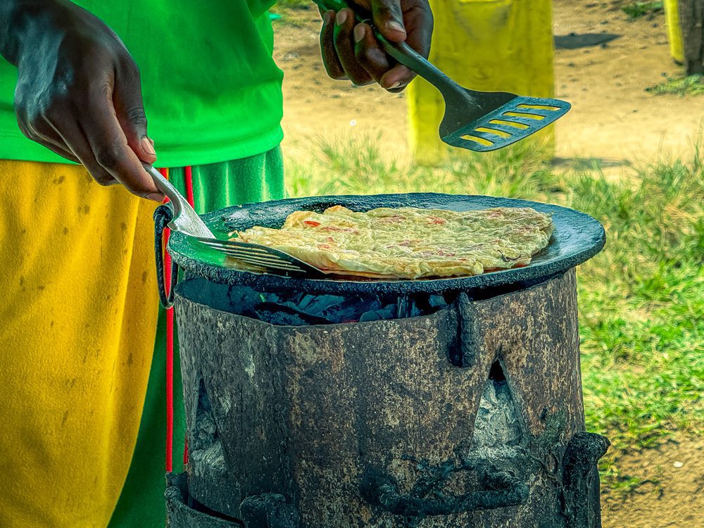 What to Eat in Uganda: A Delicious Journey Through Uganda’s Best Dishes 7 The omelette cooking on the makeshift stove with a man with green top and green and yellow shorts