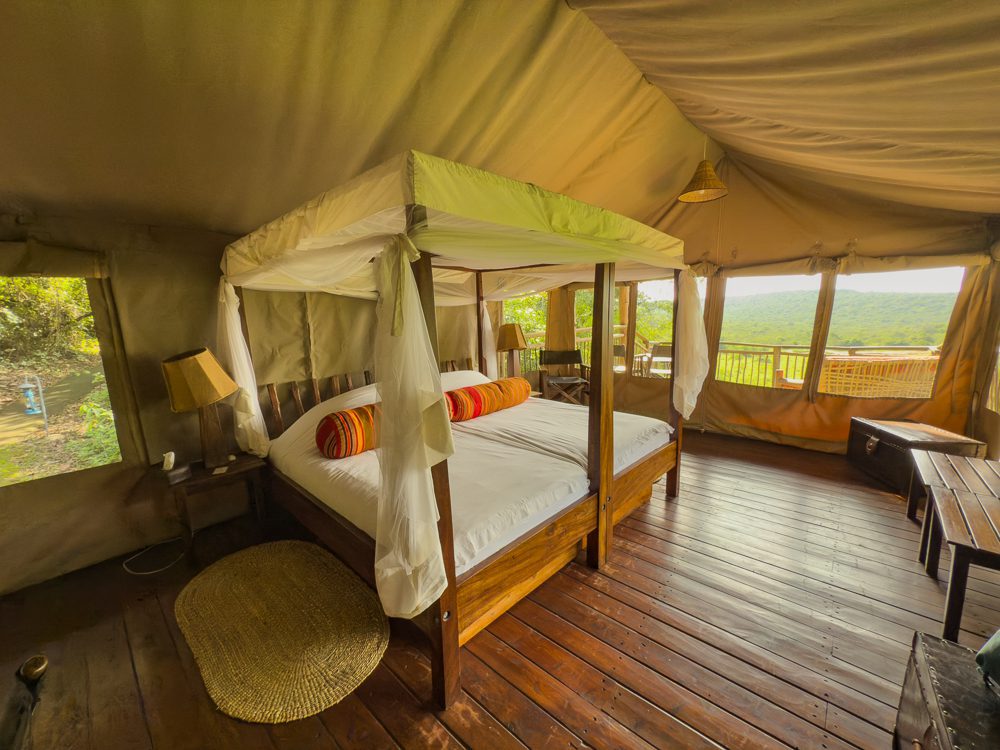 The luxurious canopied bed with amazing views with white bedding set off with red and orange stripy bolsters. there are wooden tables and a verandah