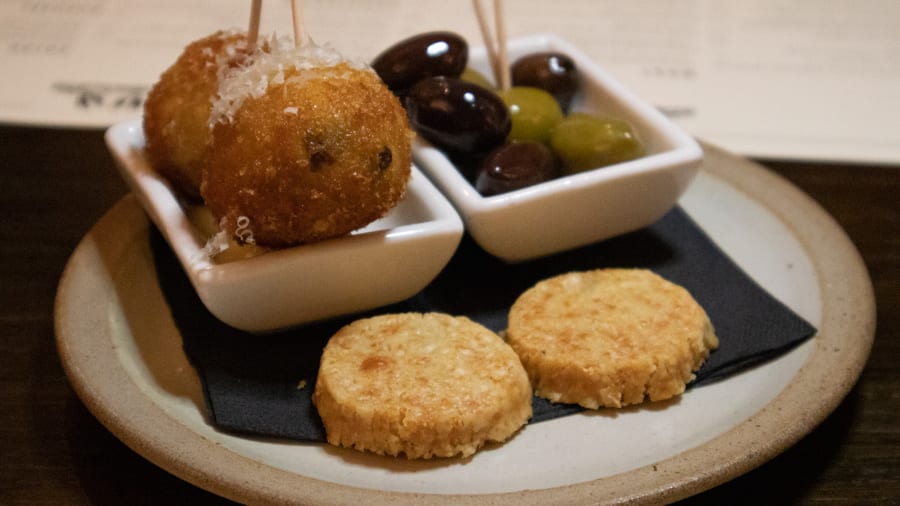 A Luxury Stay At The Angel Hotel, Abergavenny (2021) 14 Two arancini balls, green and black olives and parmesan crisps on a black napkin on a stone coloured plate