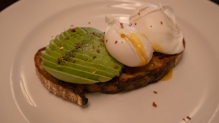 A Luxury Stay At The Angel Hotel, Abergavenny (2021) 18 sourdough toast with sliced avocado and two poached eggs topped with pepper and chilli flakes. One of the eggs is split and the yellow yolk is oozing out