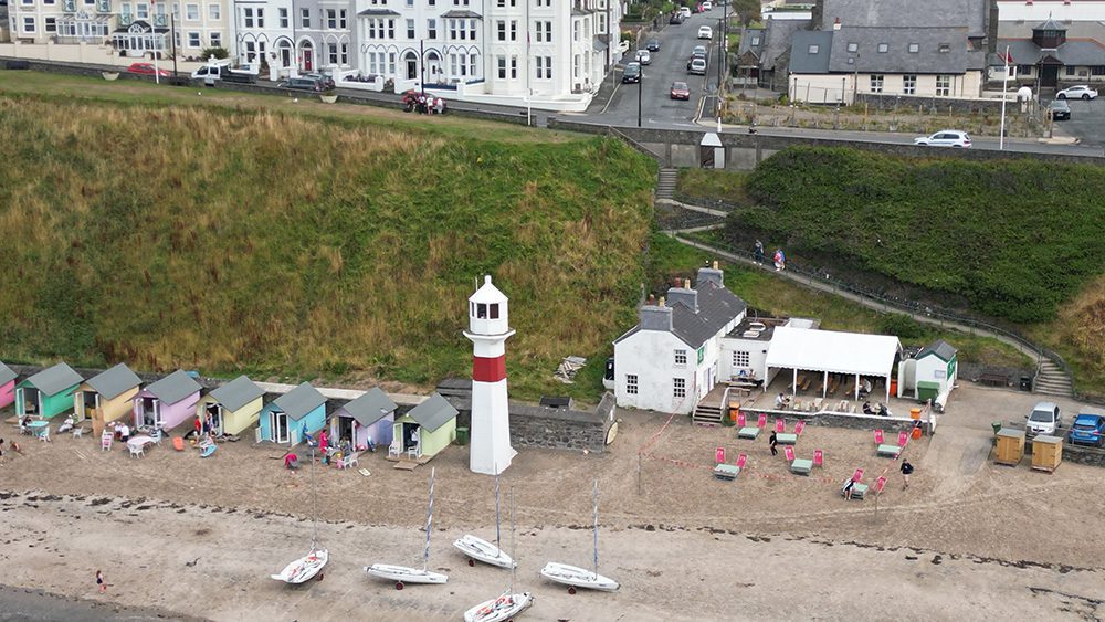 20+ Of The Best Things To Do In Port Erin, Isle Of Man 21 Foraging Vintners & Noa Bakehouse at the Cosy Nook, Port Erin beach with red and white lighthouse, pastel painted beach huts
