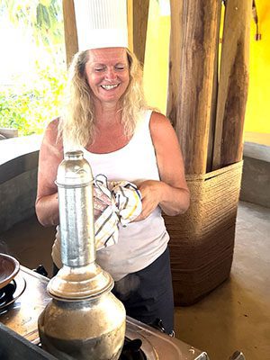 The Best Food In Sri Lanka To Eat (Including 5 Easy Recipes!) 20 silver pittu steamer with Larch behind wearing a white sleeveless tshirt and grey shorts and chefs hat